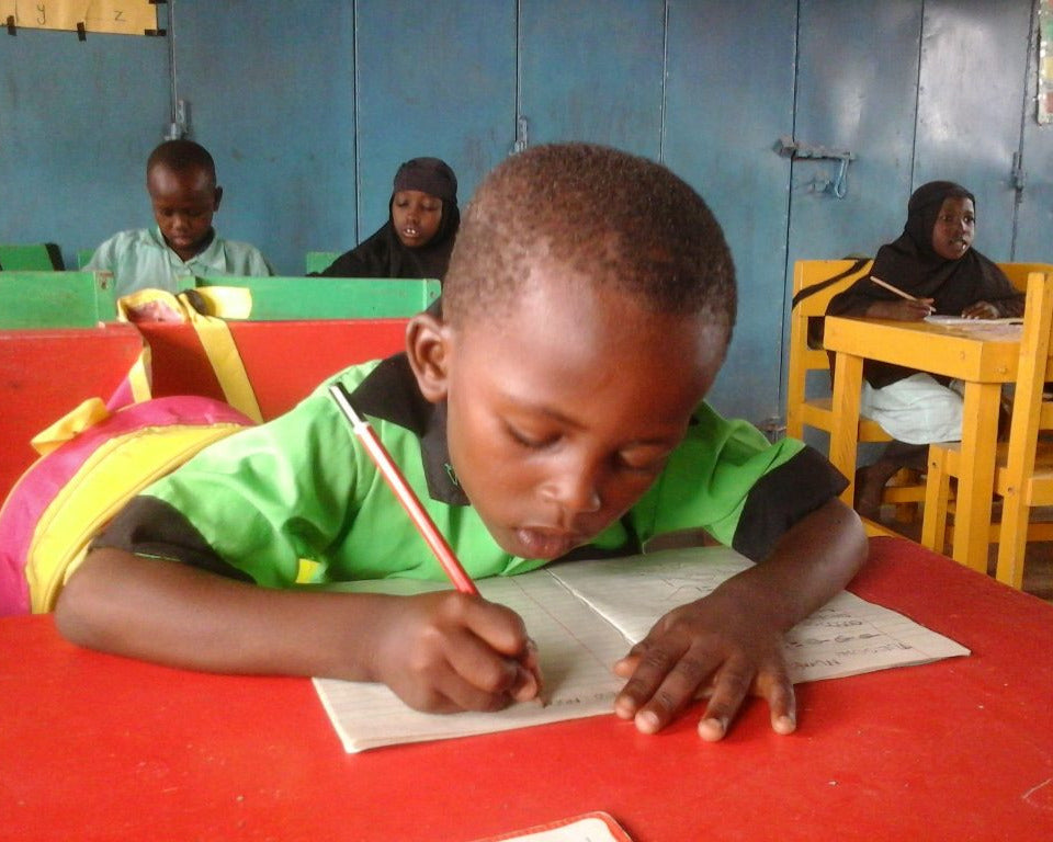 Child writing in a notebook at his bright red desk.