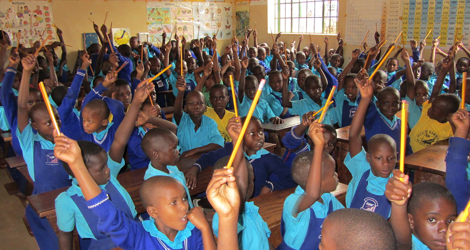 School children at Kamwokya school in Uganda, in class with raised hands and pencils