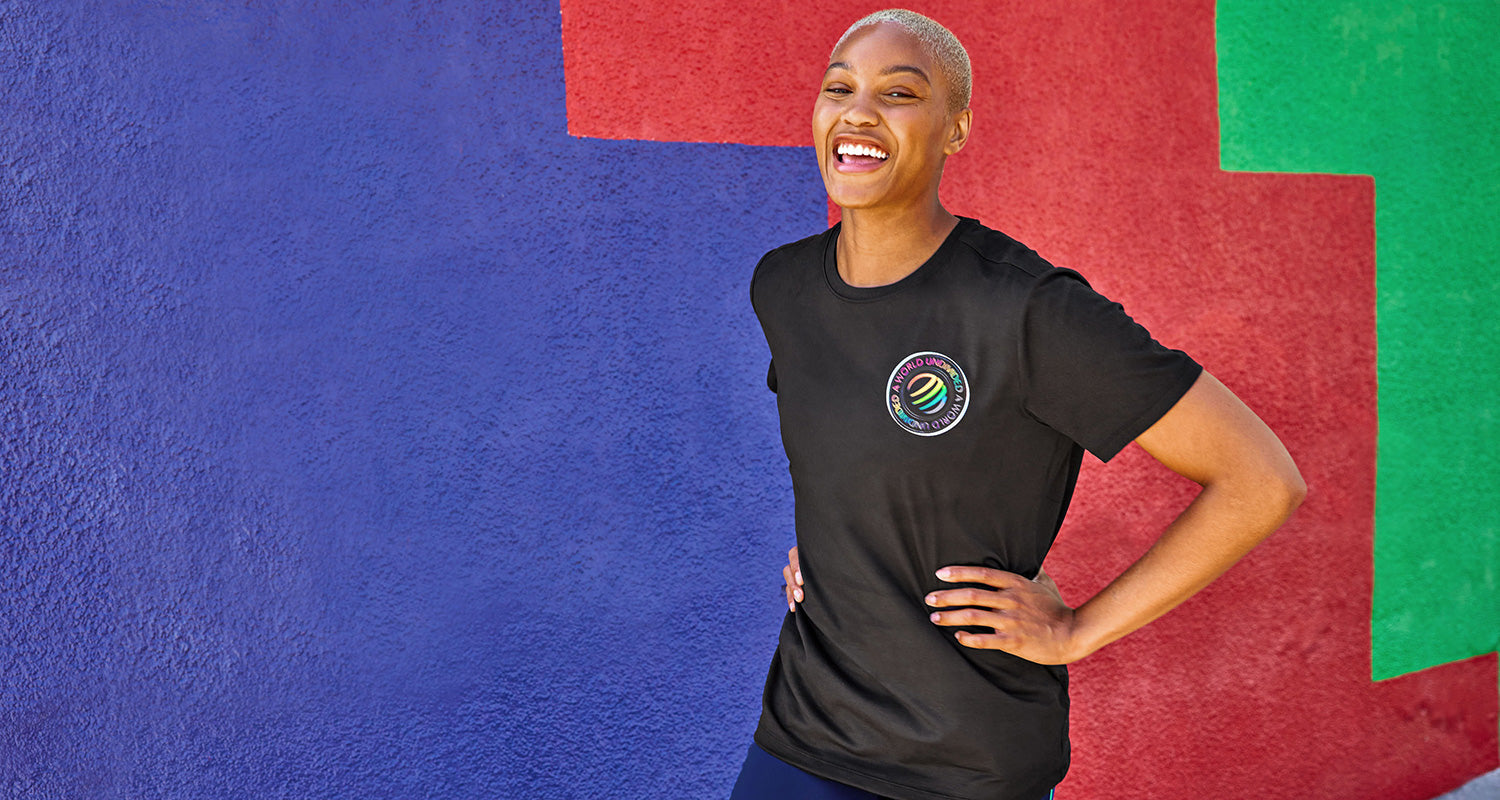 African American female wearing a black logo t-shirt in front of a multi-coloured wall
