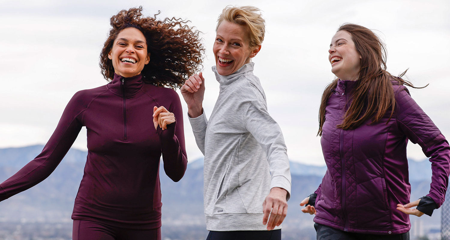 Three women in the outdoors, laughing and smiling, wearing Mondetta activewear