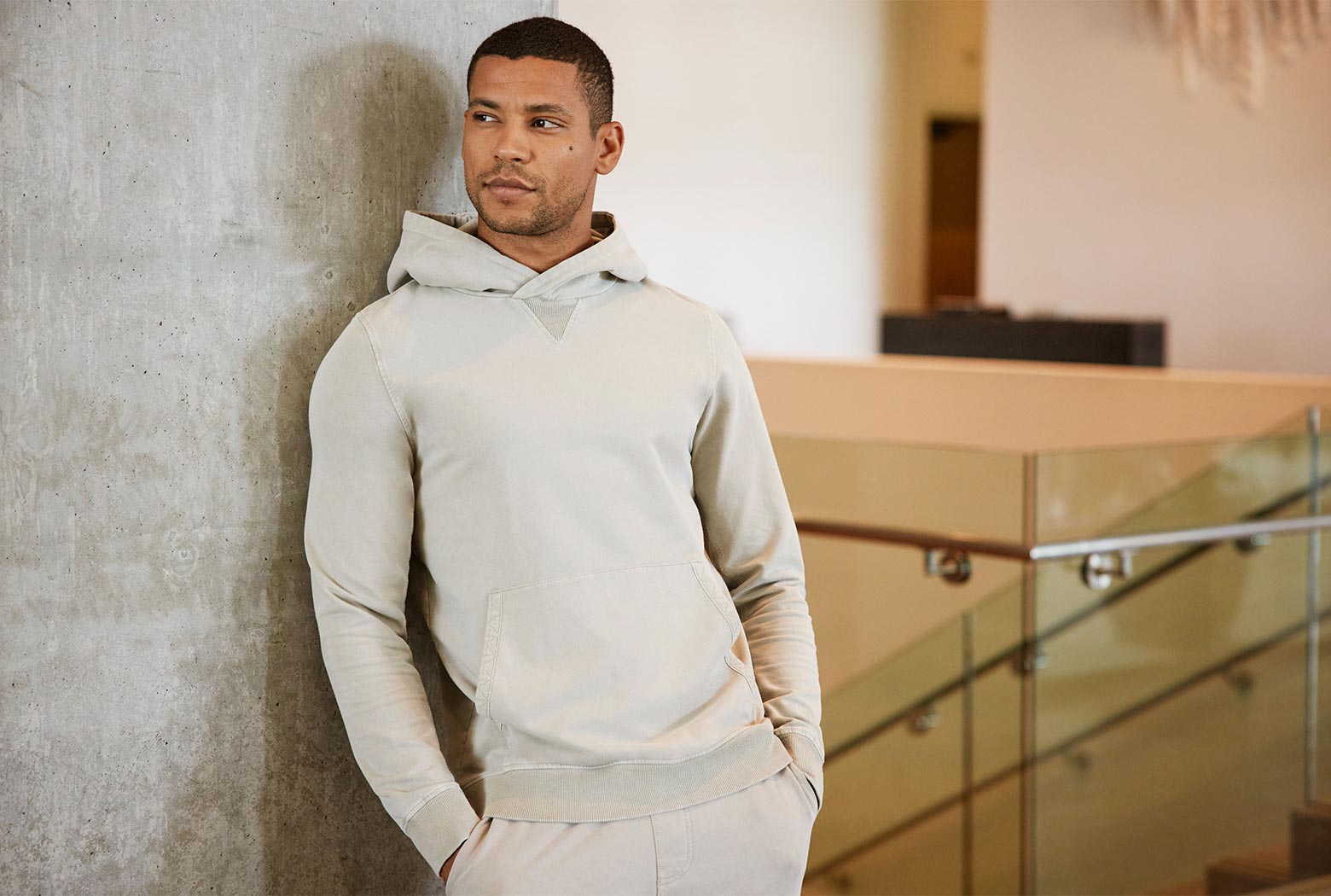 MPG male model wearing an off-white distressed sweatsuit, leaning against a wall, wide image
