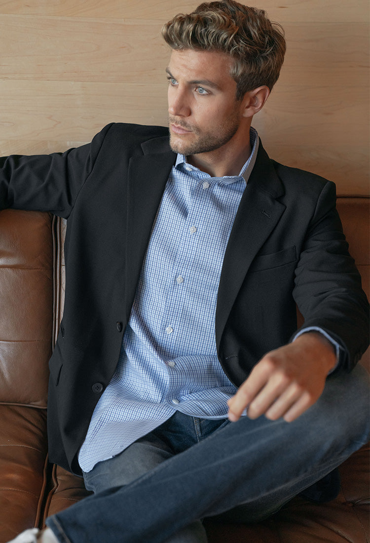 Modern Ambition male model sitting on a couch wearing a blue check dress shirt under a black blazer